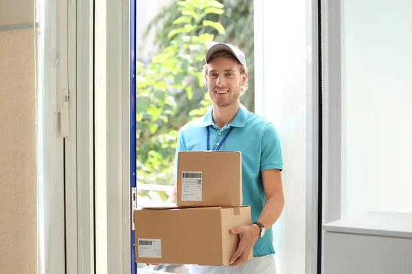 Young courier standing with parcels on doorstep