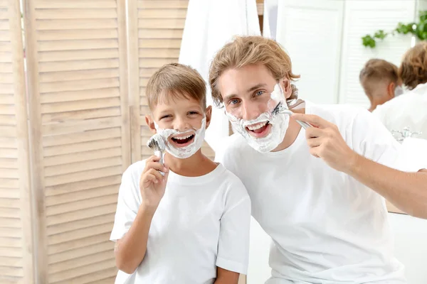 Father and son shaving together on color background
