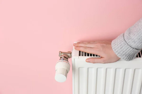 Woman warming hand on heating radiator against color background