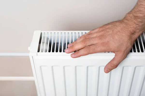 Man warming hand on heating radiator near color wall