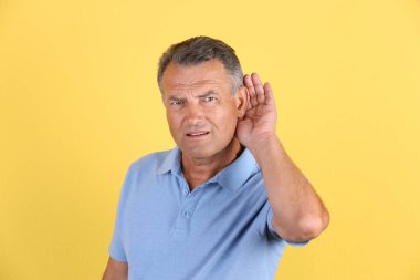 Mature man with hearing problem on color background clipart