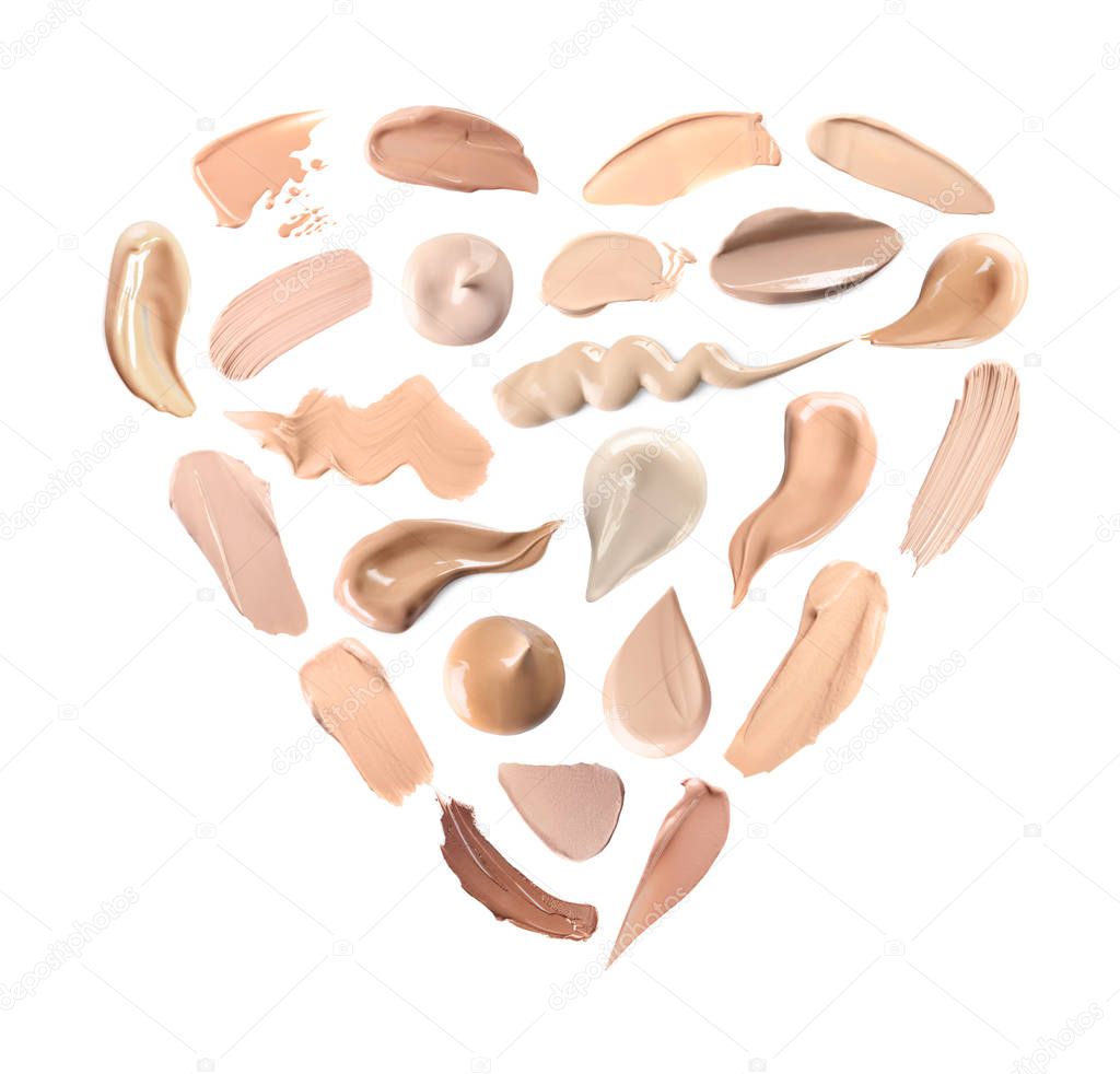 Creative set with different makeup product smears in shape of heart on white background