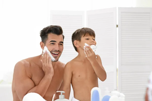 Father and son shaving on color background