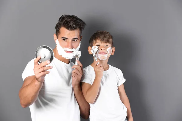 Father and son shaving on color background