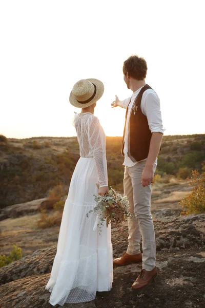 Feliz Recién Casados Con Hermoso Ramo Campo Pie Roca Atardecer —  Fotos de Stock