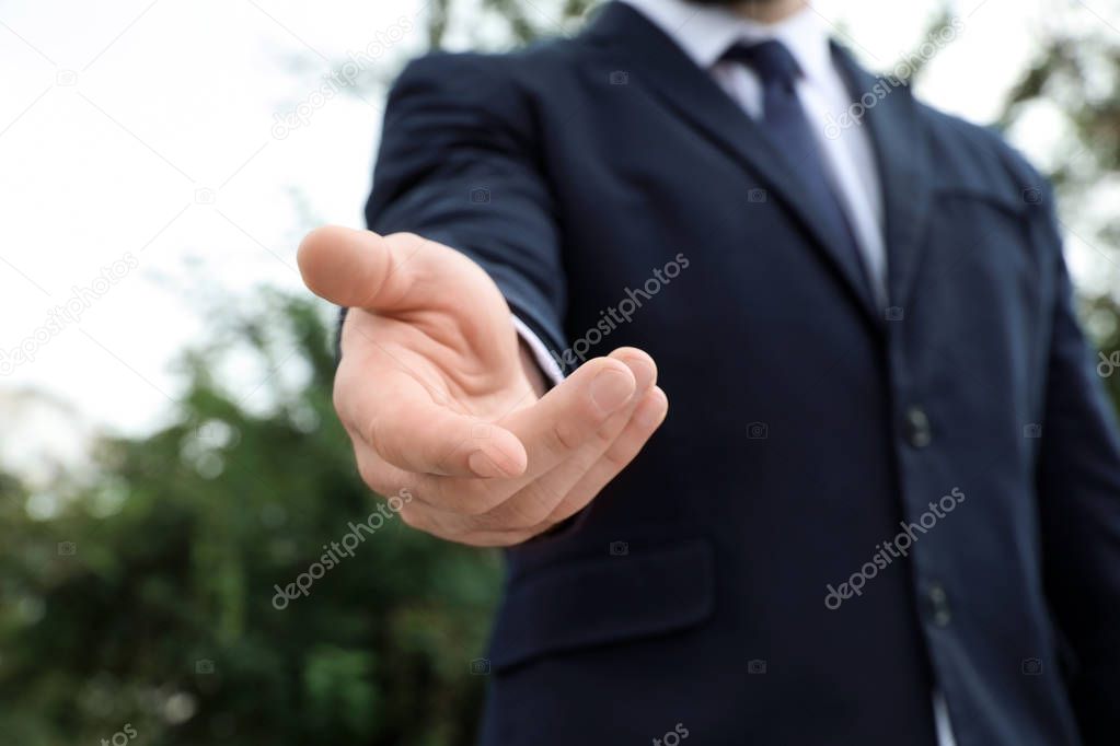 Businessman giving helping hand on blurred background outdoors