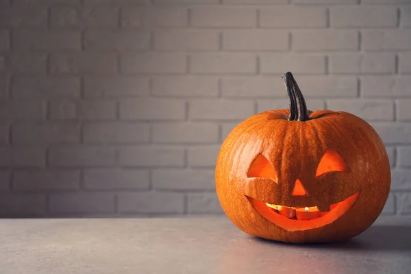 Halloween pumpkin head jack lantern on table against brick wall with space for text