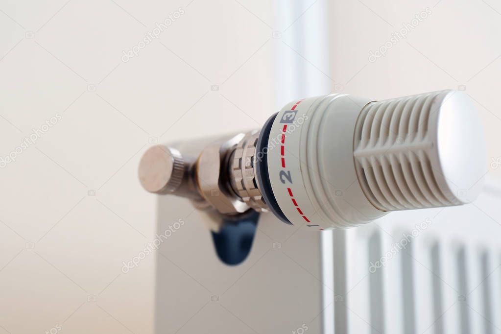 Heating radiator with thermostat near light wall, closeup