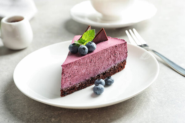 Plate with piece of tasty blueberry cake on gray table
