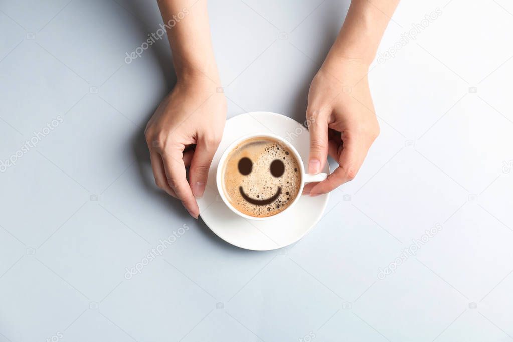 Woman holding cup of delicious hot coffee with foam and smile on light background, top view. Happy morning, good mood, inspiration