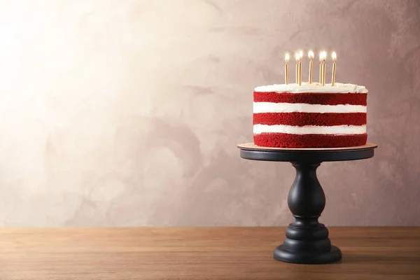Delicious homemade red velvet cake with candles on table against color background. Space for text