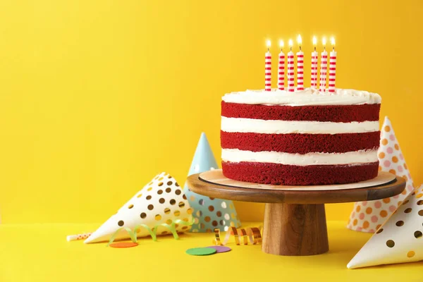 Delicious homemade red velvet cake with candles on yellow background. Space for text