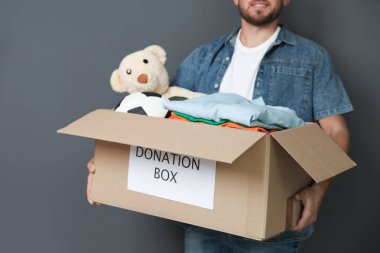 Genç adam gri arka plan üzerinde bağış kutusu holding