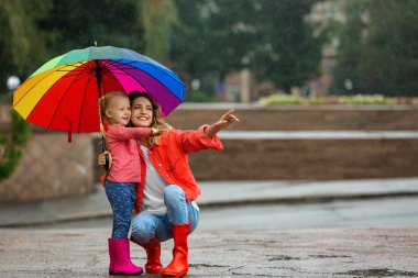 Mutlu anne ve kız açık havada yağmur altında parlak şemsiye ile