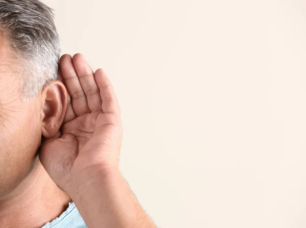 Mature man with hearing problem on light background, closeup. Space for text