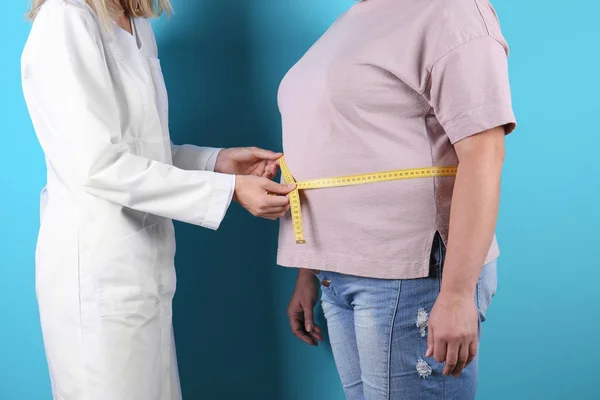 Doctor measuring fat woman\'s waist on color background. Weight loss