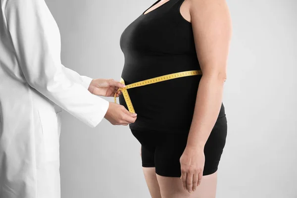 Doctor measuring fat woman\'s waist on grey background. Weight loss