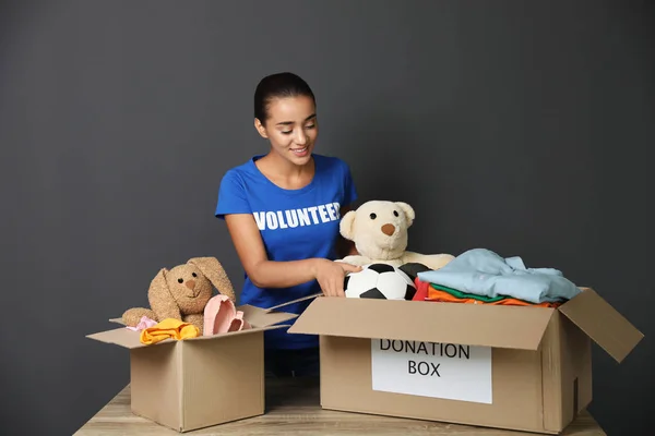 Female volunteer collecting donations at table on grey background