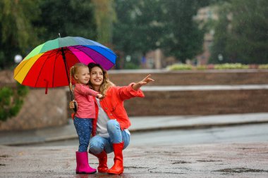 Mutlu anne ve kız açık havada yağmur altında parlak şemsiye ile