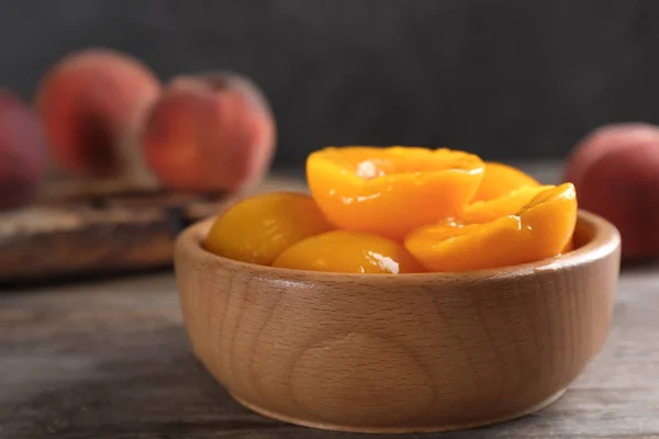 Bowl with conserved peach halves on wooden table. Space for text