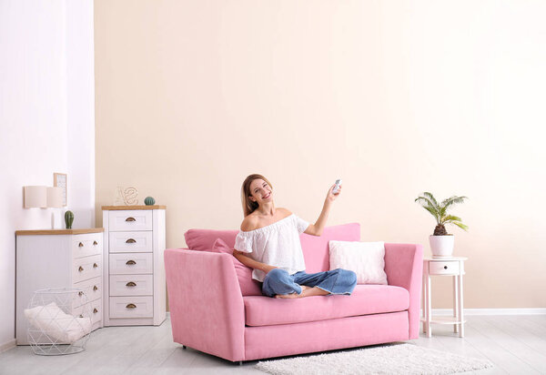 Happy young woman sitting under air conditioner at home