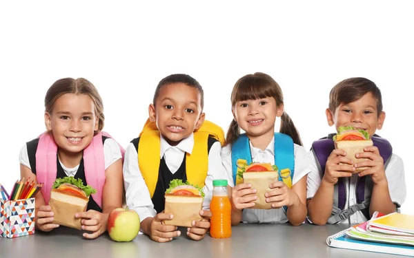 Escolares Com Alimentos Saudáveis Mochilas Sentadas Mesa Fundo Branco — Fotografia de Stock