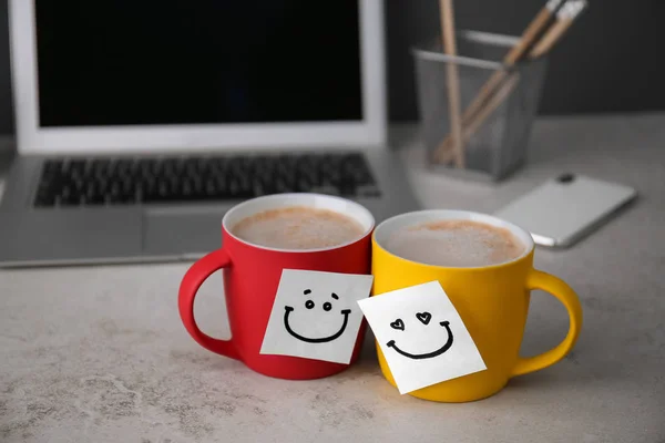 Sticky notes with funny faces attached to cups of coffee on office table. Break time