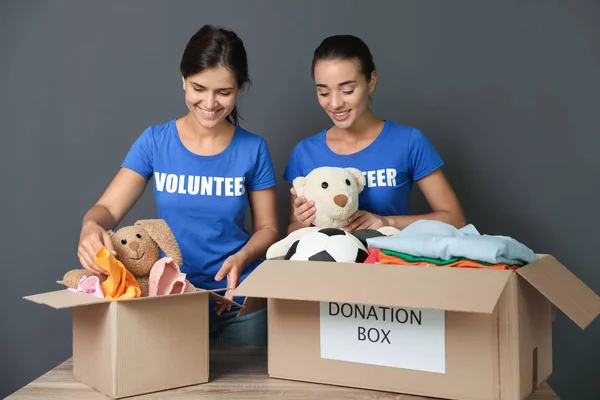 Young volunteers collecting donations at table on grey background