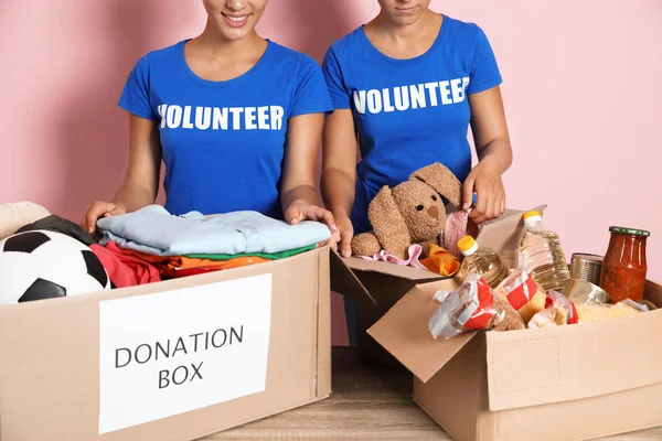 Young volunteers collecting donations at table on color background