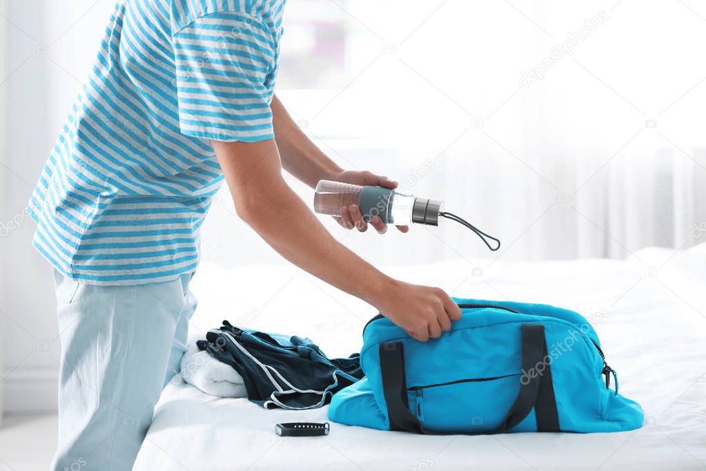 Young man packing sports stuff for training into bag in bedroom