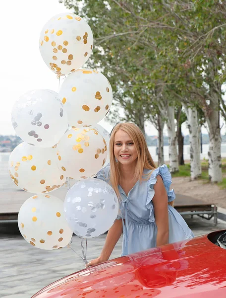 Beautiful young woman with bunch of balloons outdoors