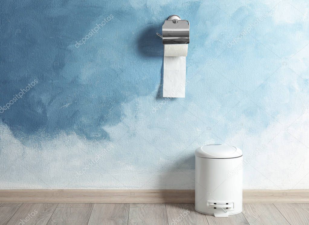 Toilet paper holder with roll and trash bin near color wall. Space for text