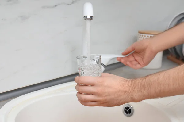 Man filling glass with water from faucet in kitchen, closeup