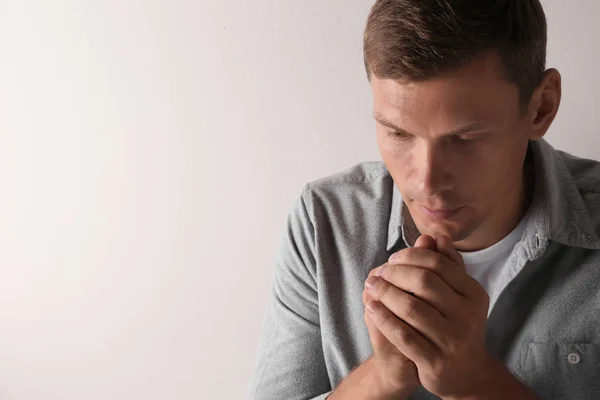 Man with hands clasped together for prayer on light background. Space for text