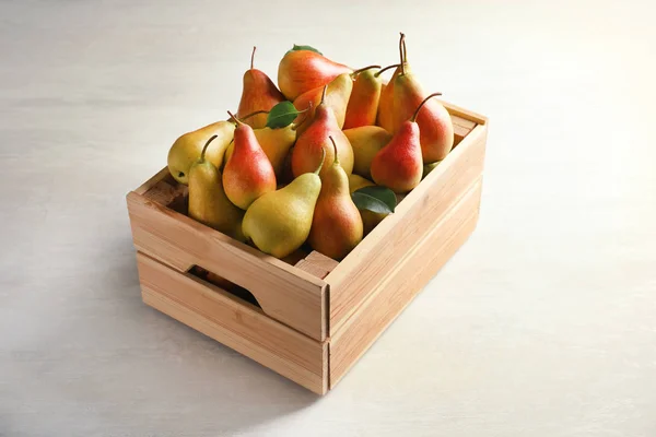 Wooden crate with ripe pears on light background