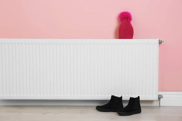 Heating radiator with knitted cap and shoes near color wall