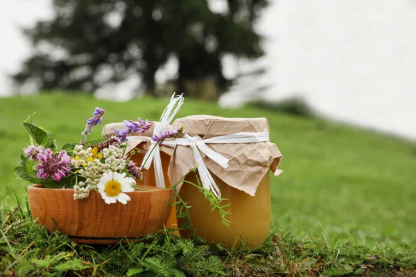 Jars with honey and flowers in bowl on green grass