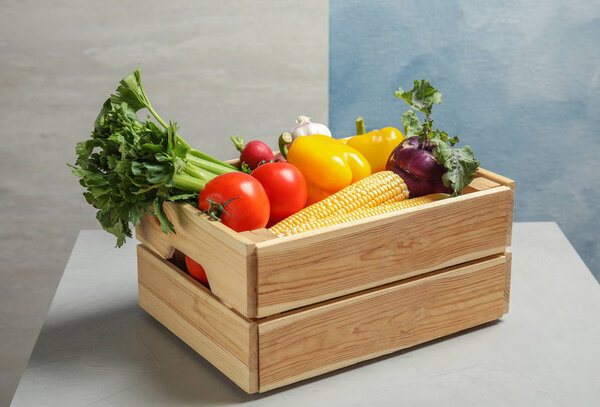 Деревянный ящик со свежими овощами на сером столе
