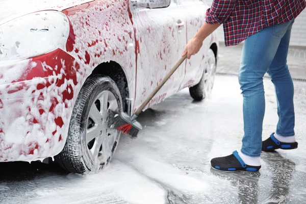 Young man cleaning vehicle with brush at self-service car wash