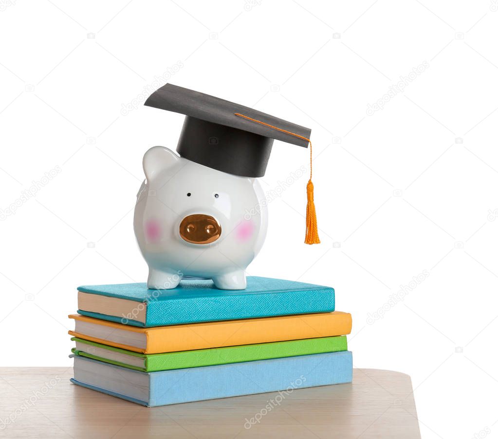 Piggy bank with graduation hat and books on table against white background