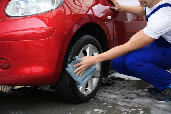 Male worker cleaning vehicle wheel with cloth at car wash