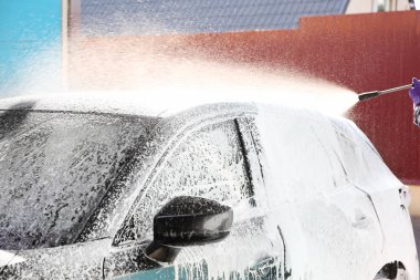 Araba yıkamada yüksek basınçlı su jeti ile otomobil temizleyen bir işçi.