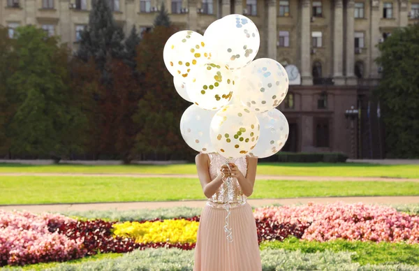 Young woman hiding behind glitter balloons on street