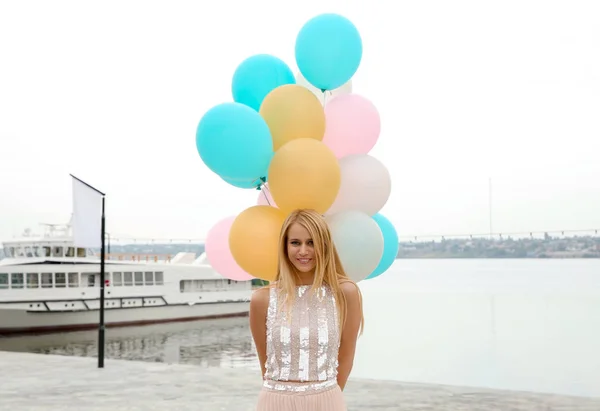 Beautiful young woman with bunch of balloons outdoors
