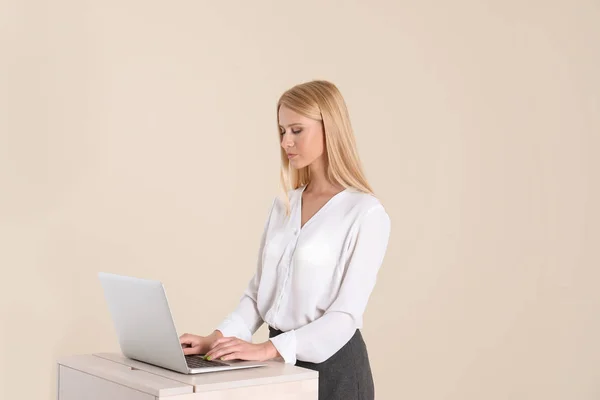 Young woman using laptop at stand up workplace against light wall