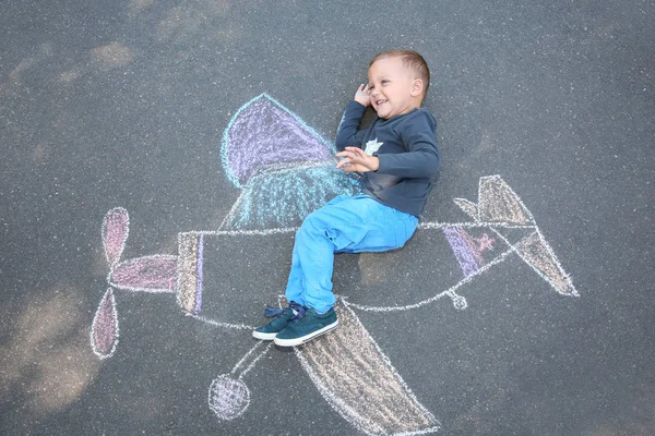 Kleines Kind Liegt Neben Kreidezeichnung Eines Flugzeugs Auf Asphalt Ansicht — Stockfoto