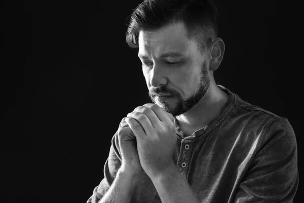 Man with hands clasped together for prayer on dark background, black and white effect. Space for text