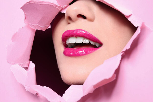 Вид красивой молодой женщины с идеальным макияжем губ через отверстие в цветной бумаге
