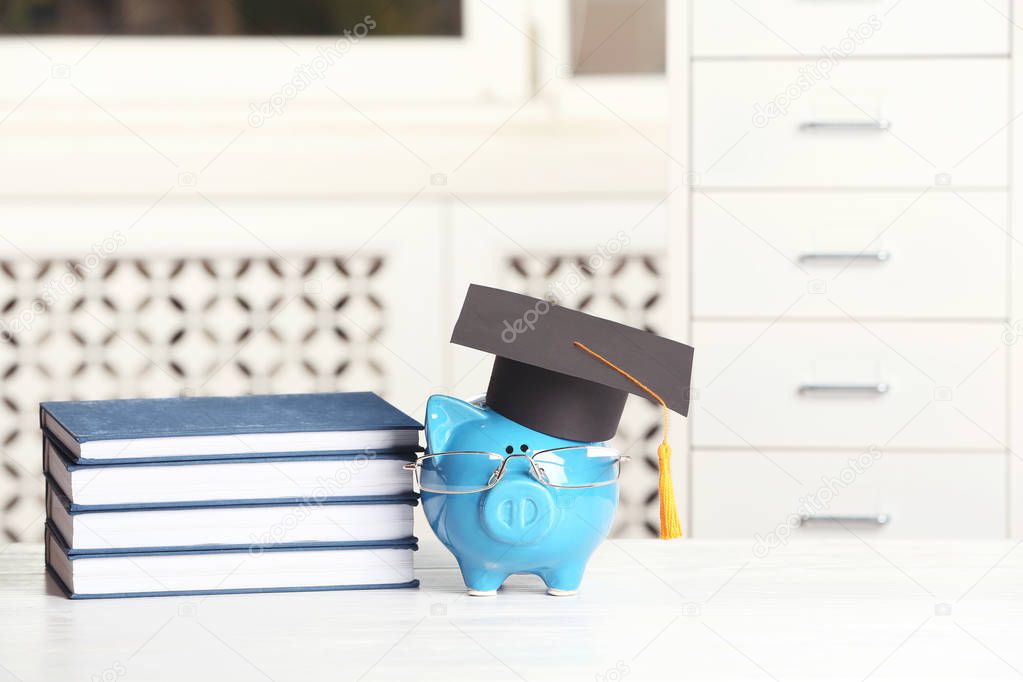 Piggy bank with graduation hat and books on table against blurred background