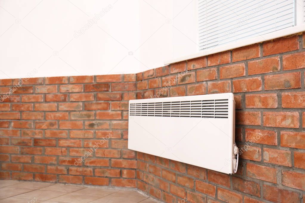 Modern heating convector on brick wall indoors